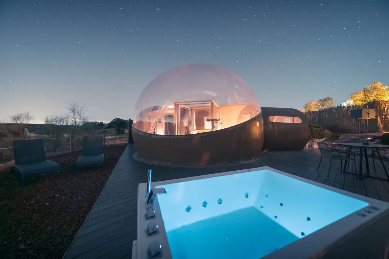 Bañera de hidromasaje exterior privada iluminada en azul en una terraza de madera, con una cúpula geodésica habitable