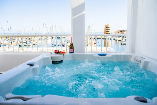Jacuzzi con agua burbujeante en una terraza privada, con una botella de champán y un plato de fresas en el borde. Al fon