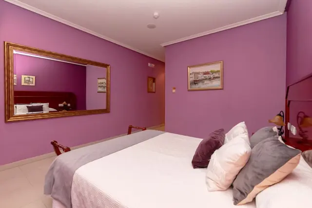 Habitación de motel con paredes pintadas de color púrpura, una cama grande con sábanas blancas y múltiples almohadas