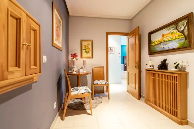 Interior de una habitación con paredes en tonos grises y beige, piso de baldosas blancas, un pequeño comedor con mesa