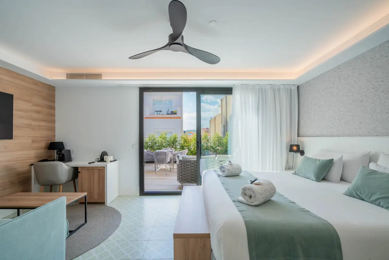 Habitación de hotel con cama doble grande vestida en blanco y verde, cojines a juego, toallas enrolladas, escritorio