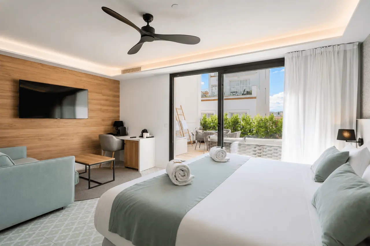 Vista de una suite de hotel con una cama grande vestida de blanco y turquesa con toallas enrolladas, un sofá azul