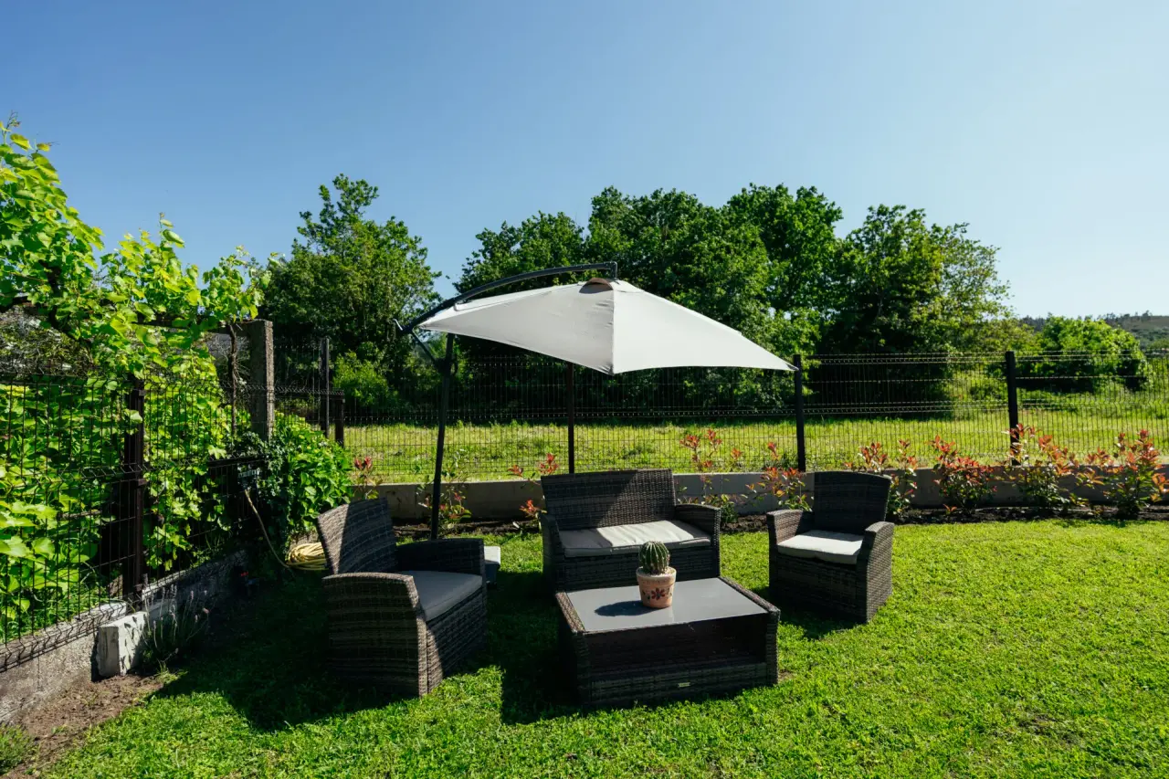Jardín exterior con césped, un conjunto de muebles de exterior de mimbre oscuro con cojines claros, una mesa baja