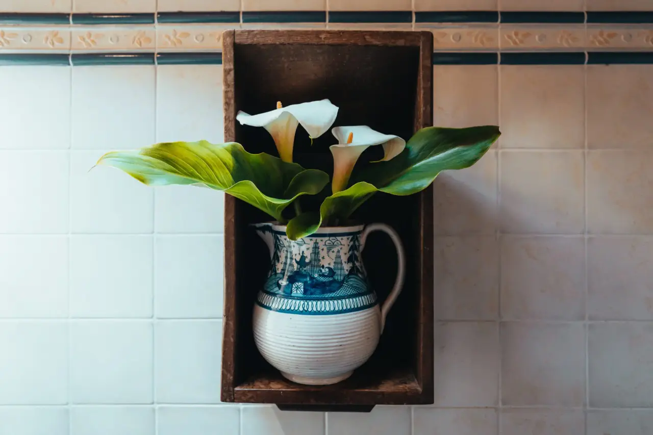 Detalle decorativo en el baño: jarra de cerámica con flores blancas colocada dentro de un nicho de madera en una pared
