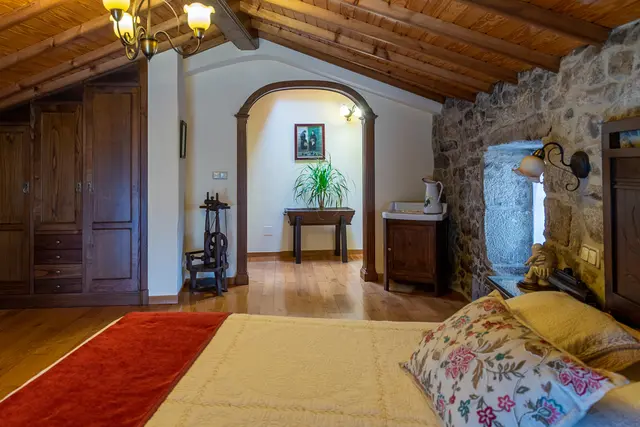 Vista de una suite con cama en primer plano, suelo de madera, techo de vigas de madera, armario empotrado, arco que da