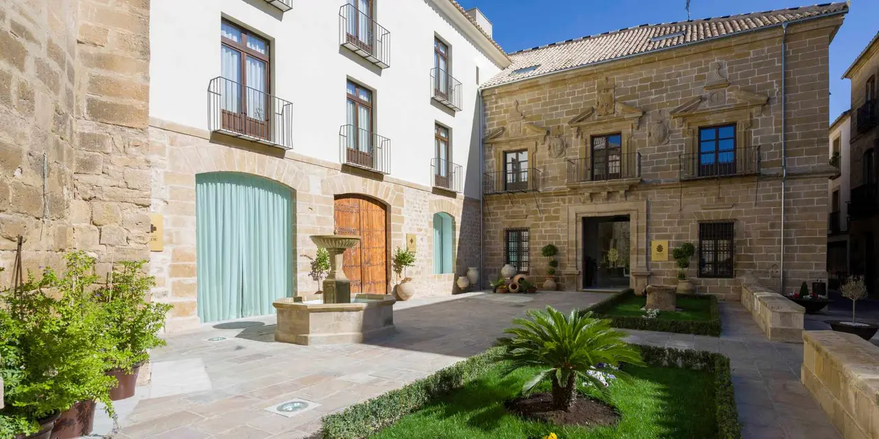 Patio interior de un edificio histórico con paredes de piedra y enlucidas en blanco, balcones con barandillas, puertas