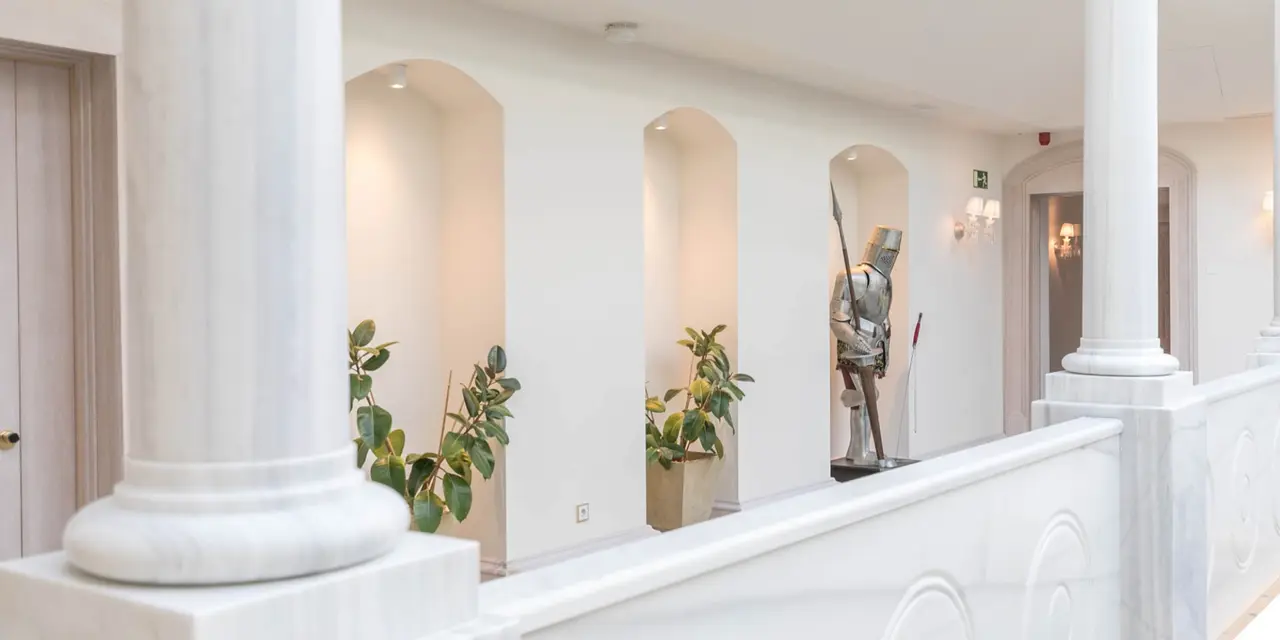 Interior de un pasillo o balcón en un edificio histórico con columnas blancas, barandilla de mármol, arcos en la pared