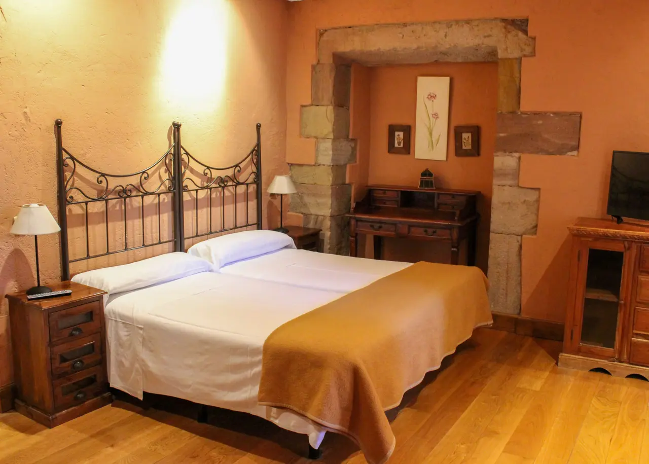 Vista de una suite de hotel con una cama doble de matrimonio con cabecero de forja, mesitas de noche con lámparas