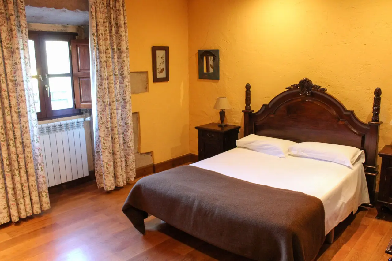 Habitación de hotel con paredes amarillas, suelo de madera, cama doble con cabecero de madera oscura y colcha marrón