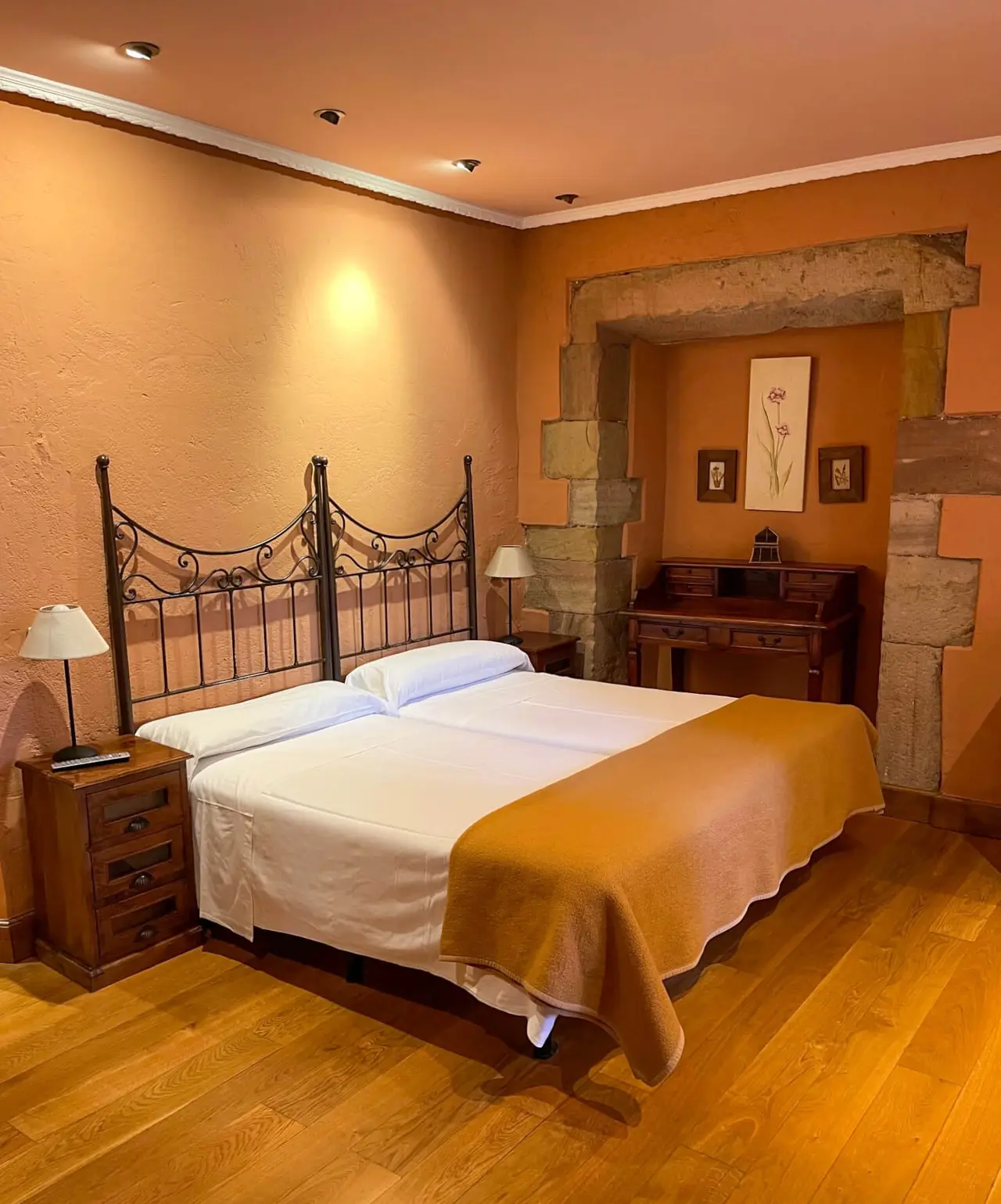 Vista de una suite de hotel con una cama doble de matrimonio con cabecero de forja, mesitas de noche de madera