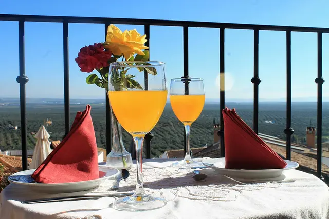Mesa para dos personas en un balcón con mantel blanco, dos copas de zumo de naranja, servilletas rojas dobladas