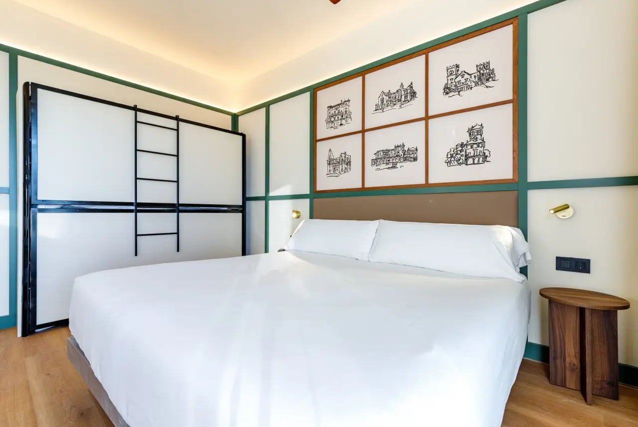Vista de una junior suite con cama doble grande vestida de blanco, cabecero acolchado, mesita de noche redonda