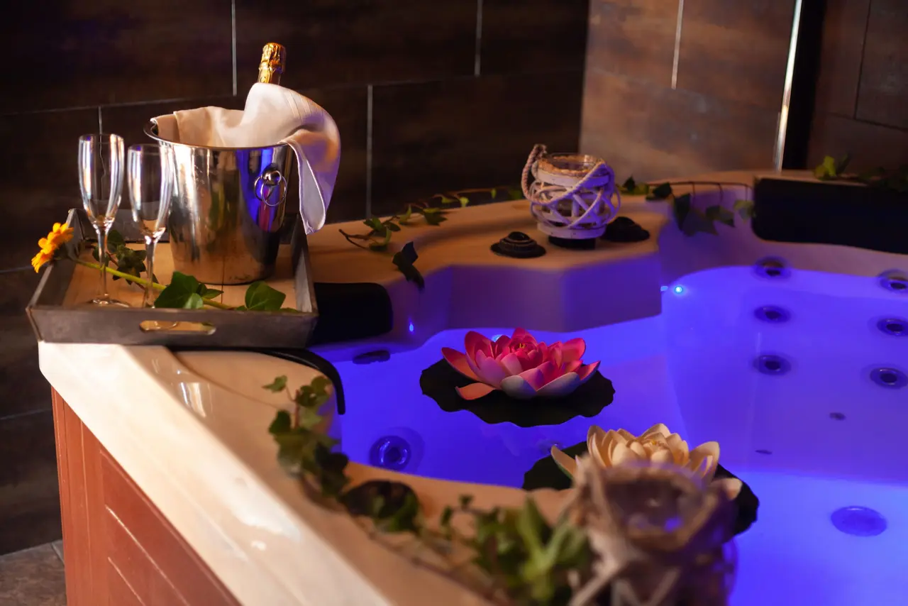 Jacuzzi interior iluminado con luz azul, decorado con flores de loto flotantes, hiedra y una bandeja con cubitera