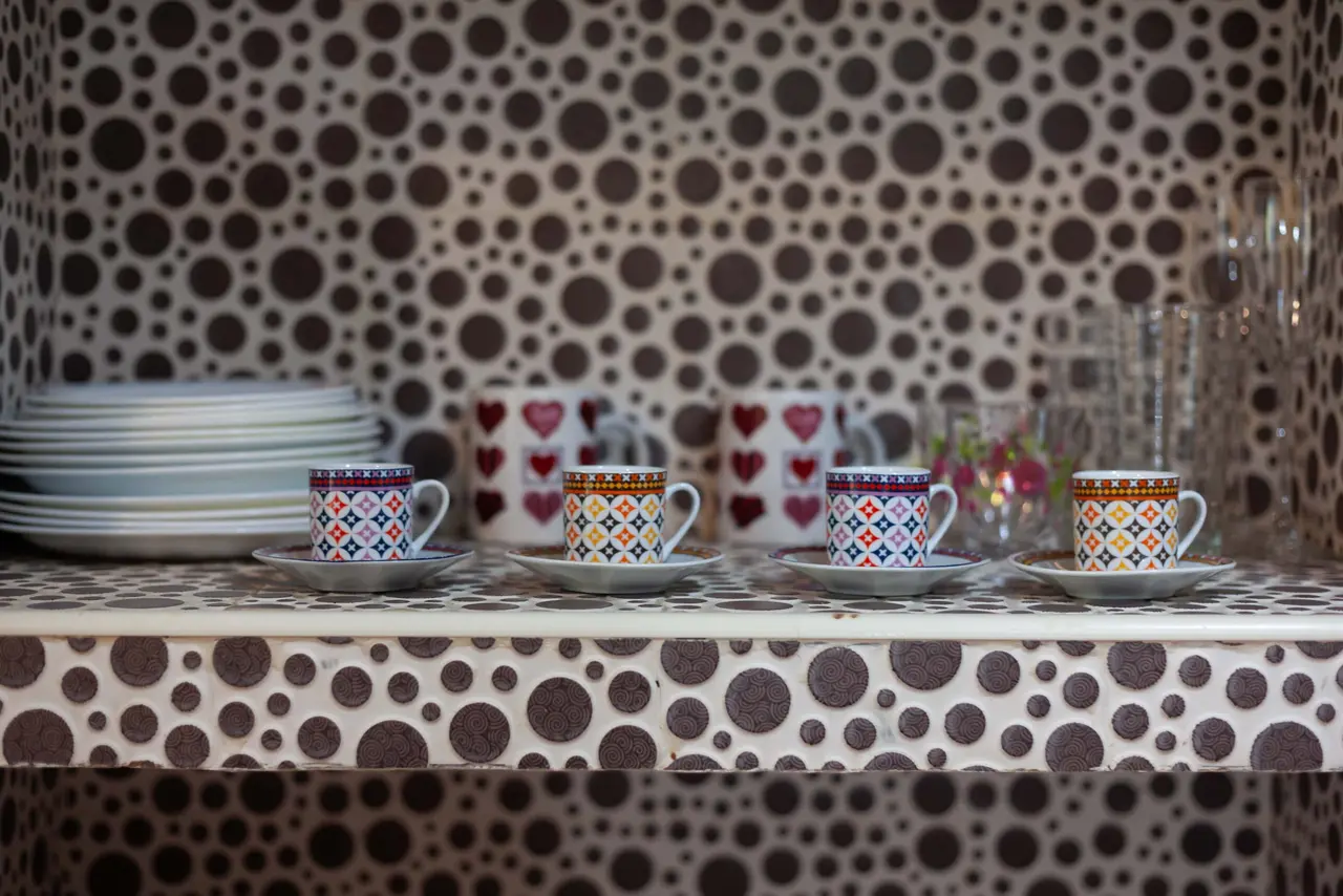 Cuatro tazas de café con sus platillos alineadas sobre una encimera de azulejos con patrón de lunares