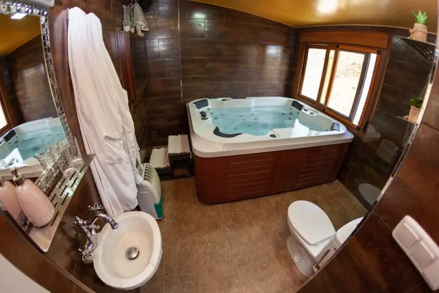 Jacuzzi rectangular empotrado en un baño con paredes de madera oscura, agua burbujeante, inodoro blanco al lado