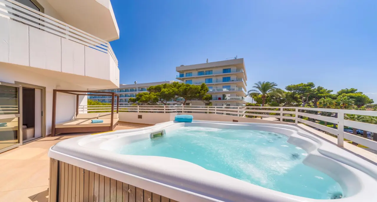 Jacuzzi privado en terraza de suite con agua azul burbujeante, rodeado de barandilla blanca, con vistas a otros