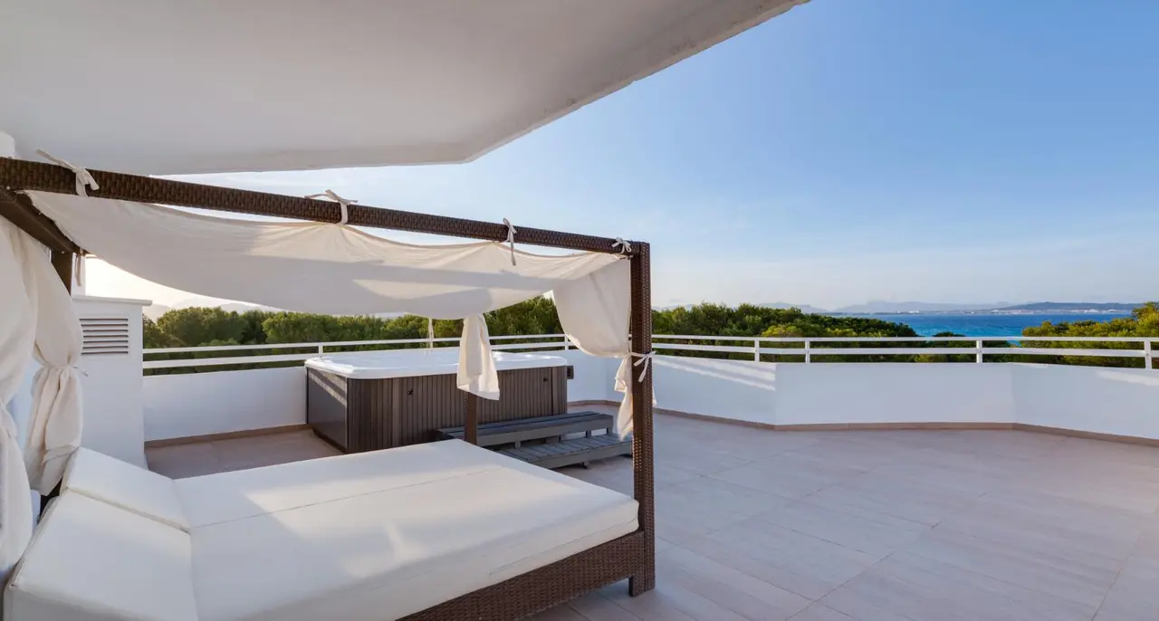 Terraza exterior con cama balinesa de madera y dosel blanco, jacuzzi privado rectangular de madera y vistas al mar