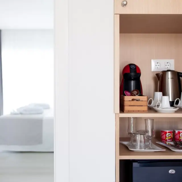 Vista parcial de una habitación de hotel con una cama al fondo a la izquierda y, a la derecha, un mueble de madera