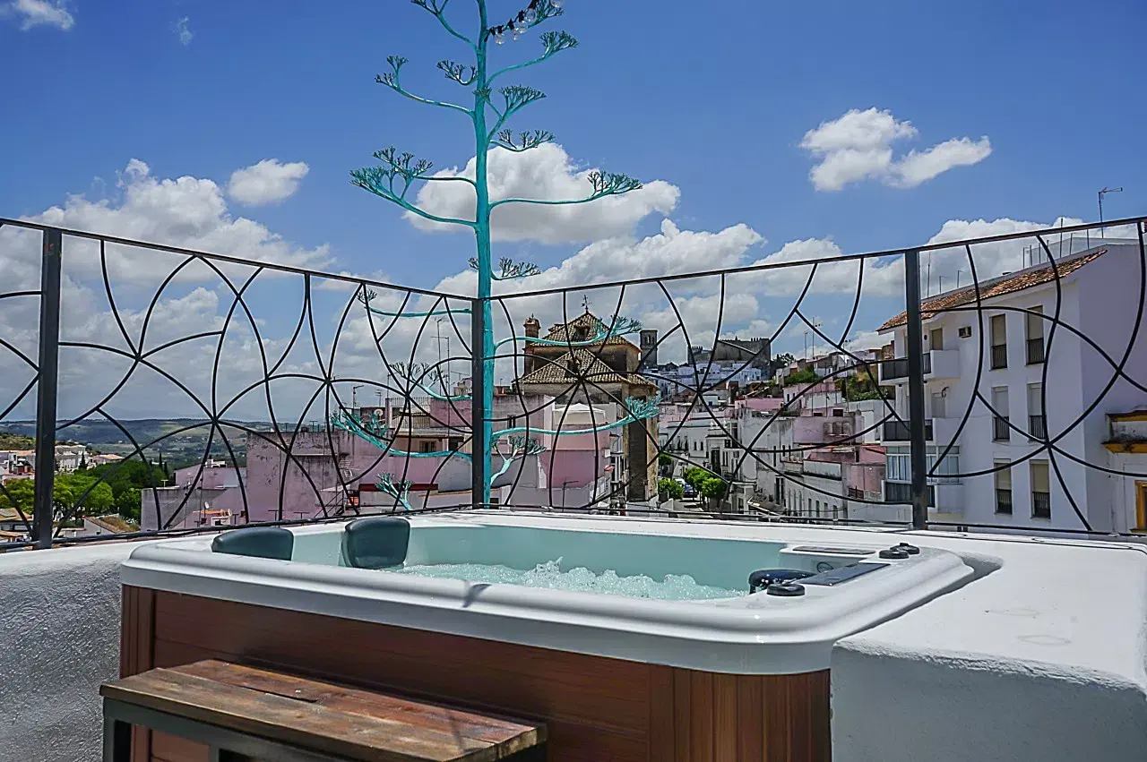 Jacuzzi en terraza privada con burbujas, rodeado de barandilla decorativa, con vistas a un pueblo con edificios