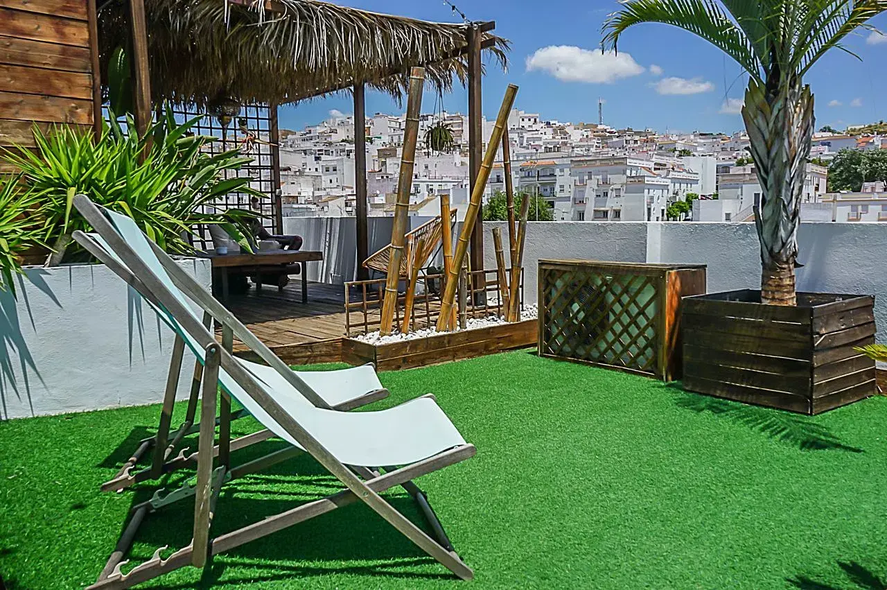 Terraza exterior con césped artificial, dos tumbonas de madera y tela, palmera en maceta de madera, pérgola con techo