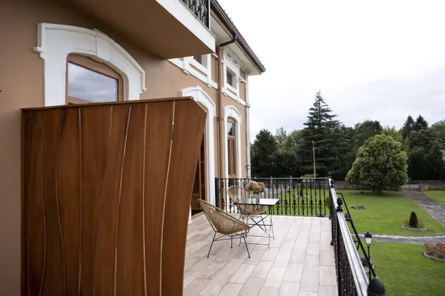 Balcón de suite con suelo de baldosas, mesa y sillas de mimbre, barandilla de hierro forjado y vistas al jardín
