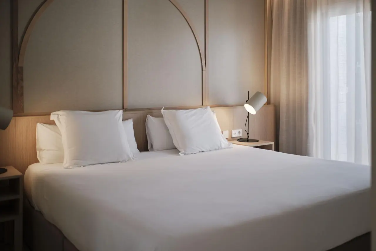Habitación con cama grande vestida de blanco, cabecero de madera con diseño arqueado, mesitas de noche y lámparas