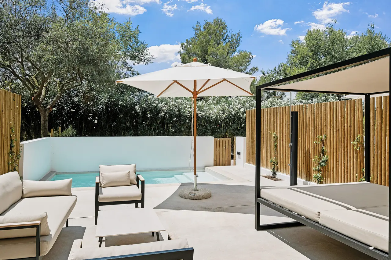 Patio exterior con piscina privada rectangular de agua azul, rodeada de suelo de hormigón claro, mobiliario