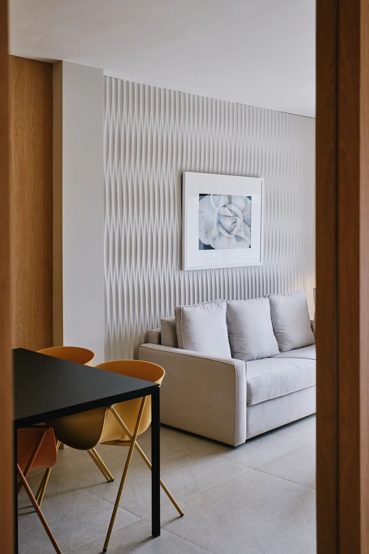 Interior de una suite con sofá claro de tres plazas, mesa negra con sillas amarillas, pared decorativa con textura
