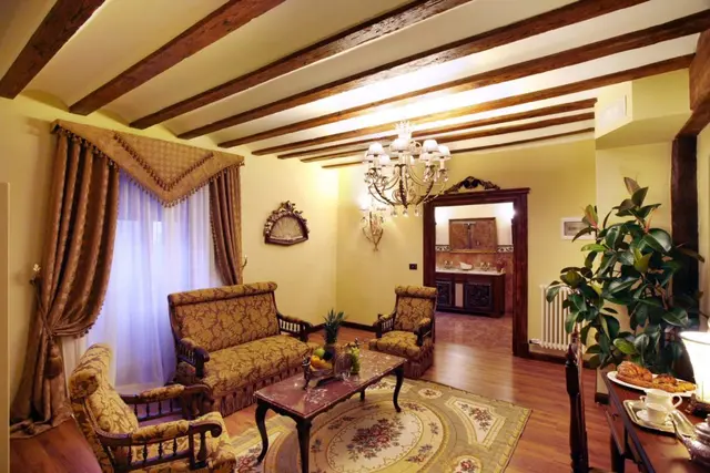 Sala de estar con sofás antiguos, mesa de centro, alfombra, lámpara de araña, techo con vigas de madera y puerta