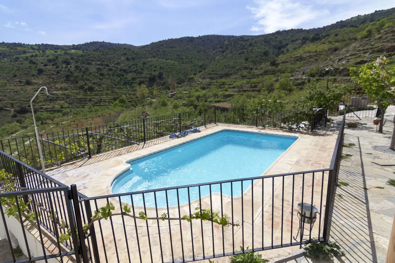 Vista de una piscina rectangular con agua azul clara, rodeada de una terraza de piedra y barandilla negra