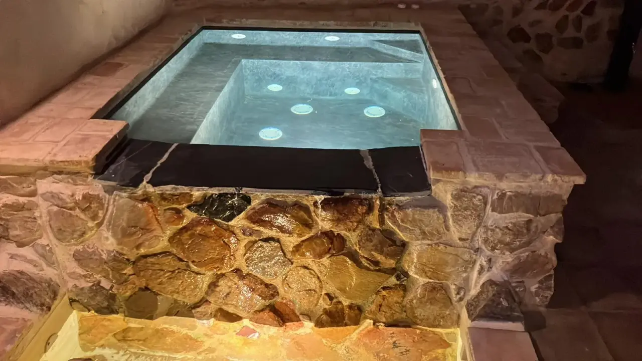 Jacuzzi rectangular empotrado en el suelo, con borde de piedra natural y azulejos, iluminado desde abajo con luz