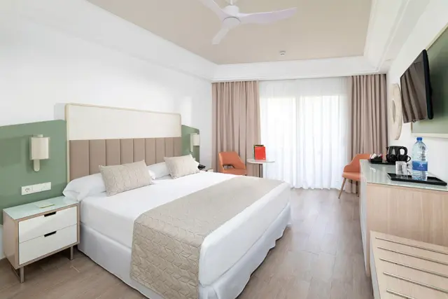 Habitación de hotel con cama king size vestida de blanco, cabecero acolchado, mesitas de noche, escritorio