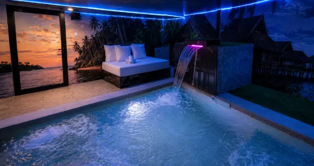Piscina privada climatizada en el interior de una habitación, con agua iluminada en azul, cascada iluminada en rosa