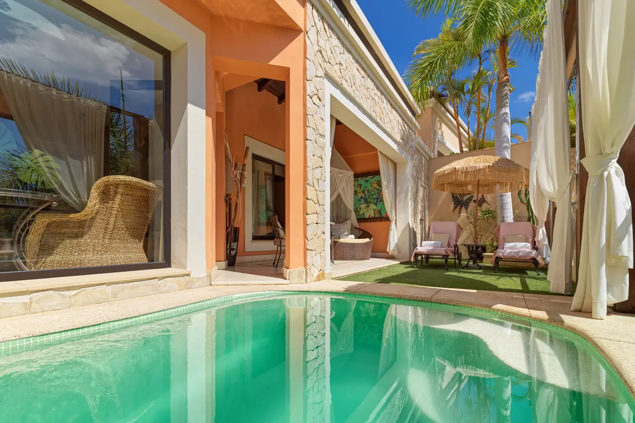 Piscina privada con agua turquesa en el patio de una villa, rodeada de césped, tumbonas con dosel, una sombrilla
