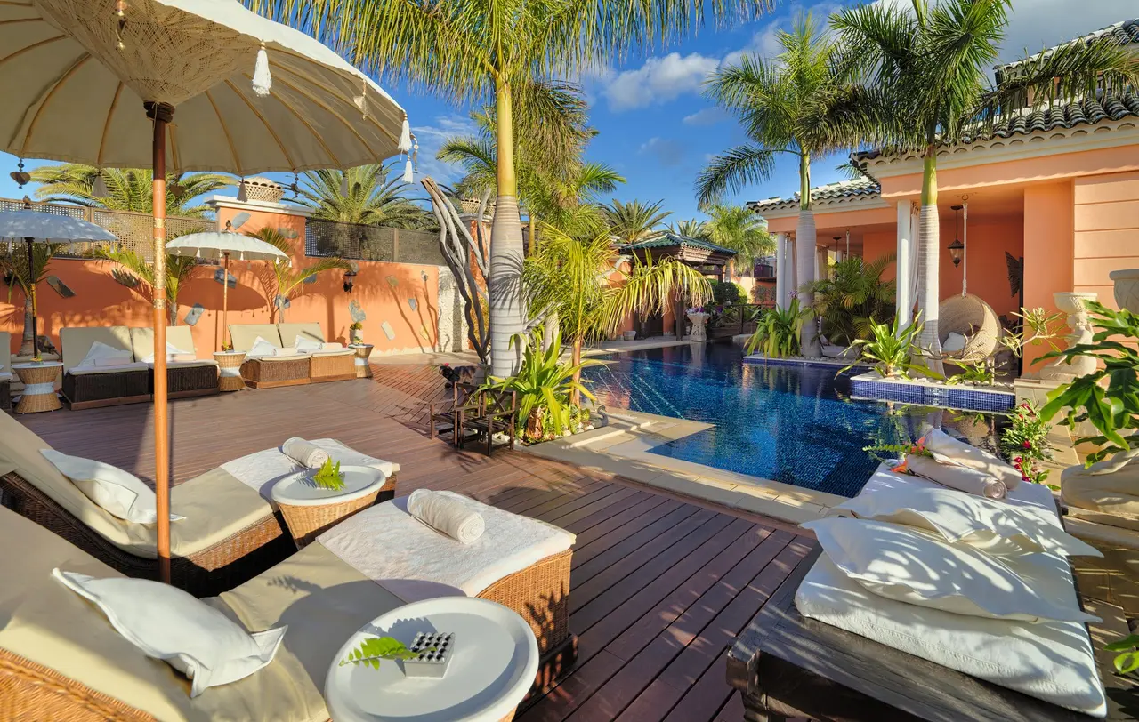 Piscina privada rectangular con agua azul en una villa, rodeada de una amplia terraza de madera con tumbonas