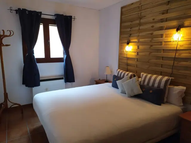 Habitación con cama doble cubierta por edredón blanco, cabecero de pared de madera horizontal, varios cojines