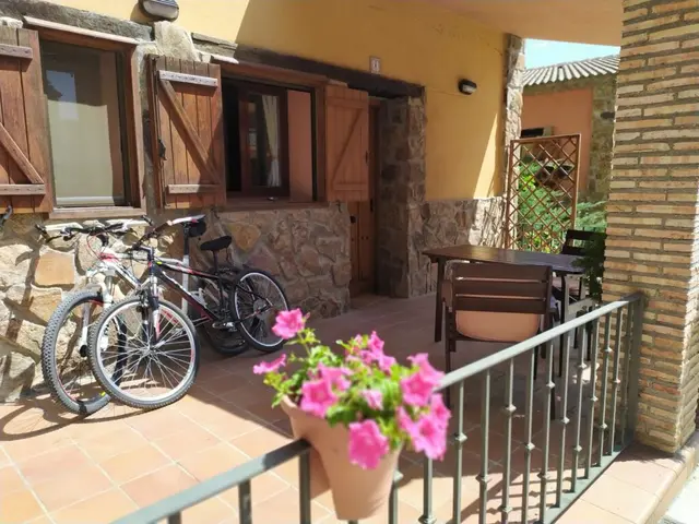 Terraza exterior de una cabaña rural con suelo de terracota, barandilla metálica, mesa y sillas de exterior