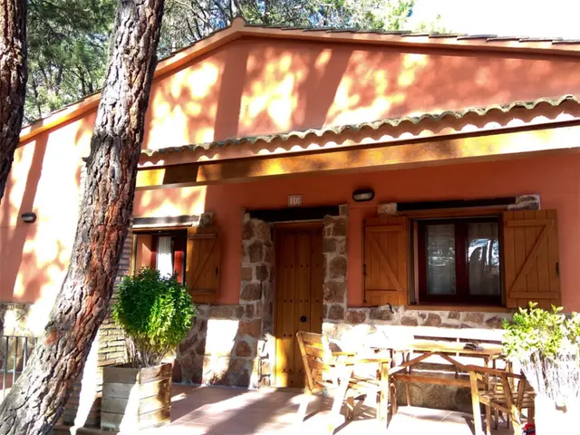 Fachada exterior de una cabaña rural con paredes de color salmón y base de piedra, puerta de madera, ventanas