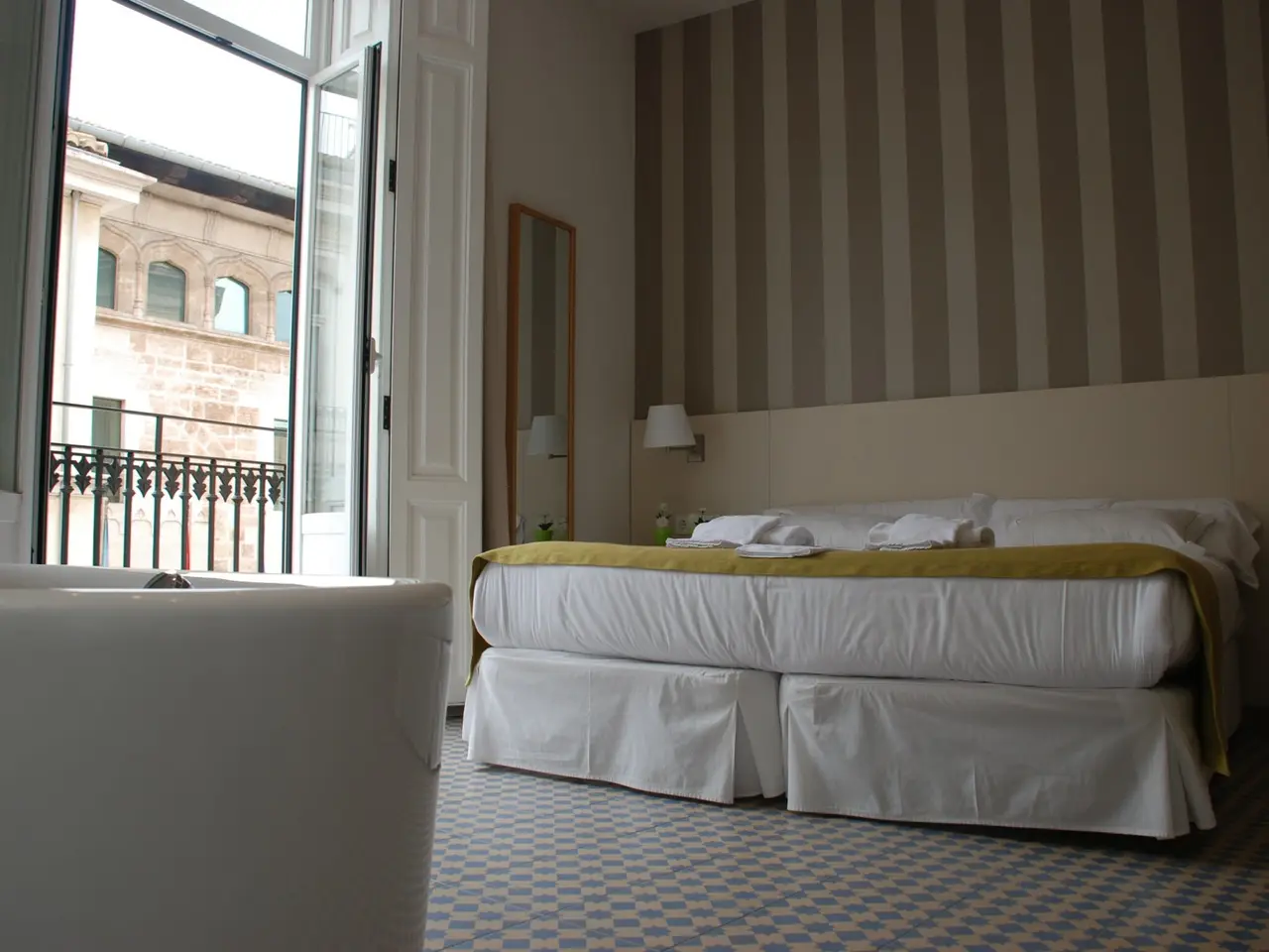 Habitación doble con cama grande vestida de blanco, una bañera blanca de hidromasaje en primer plano, suelo