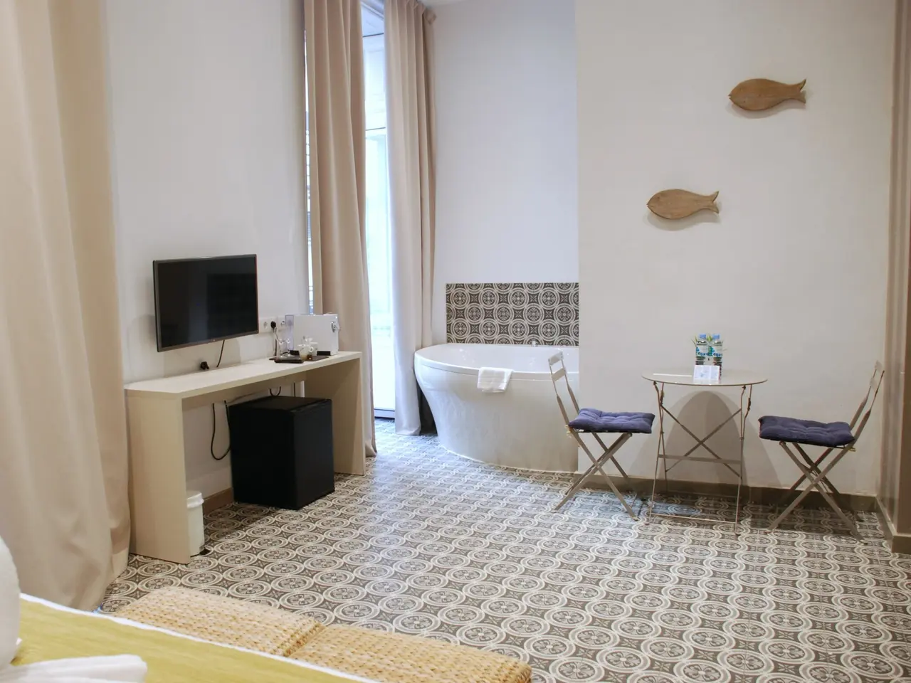 Habitación de hotel con una bañera blanca tipo jacuzzi en una esquina, escritorio con televisor, mesa redonda