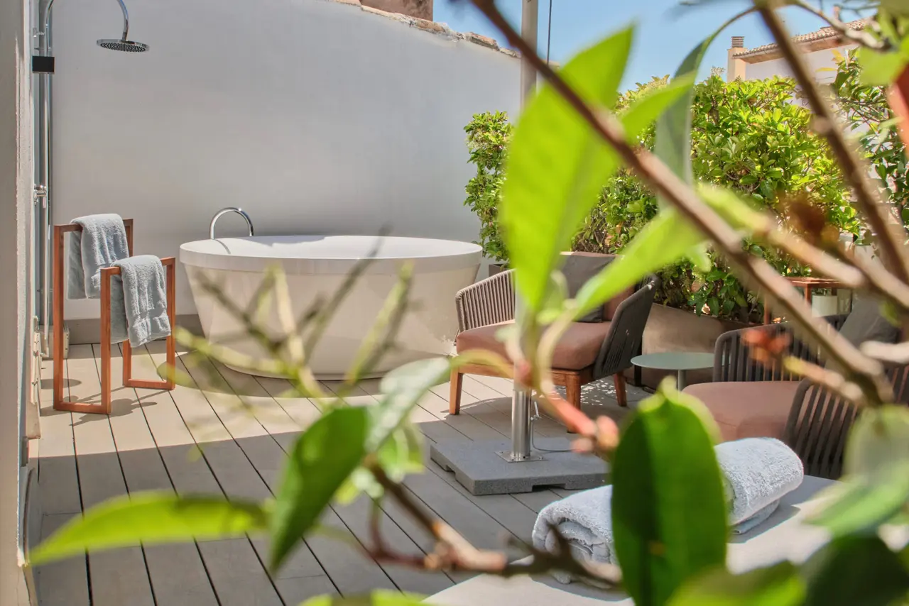 Bañera exenta de jacuzzi en terraza privada con ducha, tumbonas y vegetación.