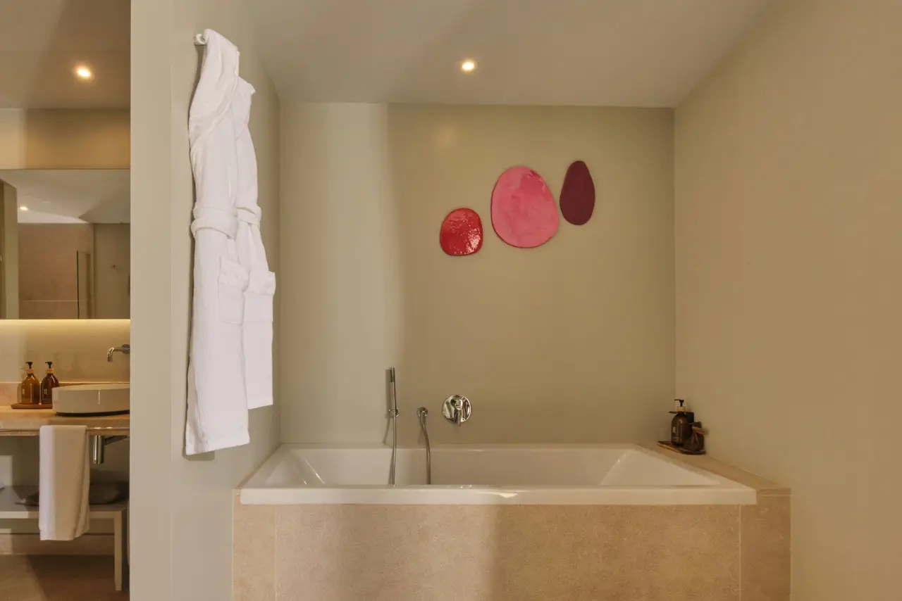 Baño con bañera empotrada, albornoz colgado y decoración de círculos rosados en la pared.