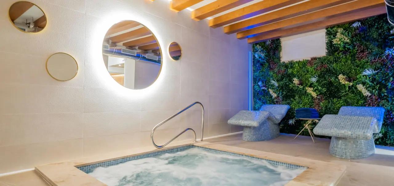 Baño con bañera de hidromasaje rectangular empotrada en el suelo, rodeada de azulejos claros, con barandilla metálica