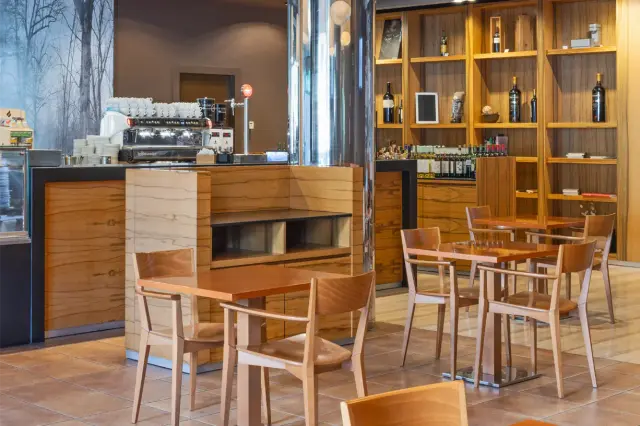 Interior de un bar o cafetería con mostrador de madera, máquina de café espresso, estanterías con botellas y estantes