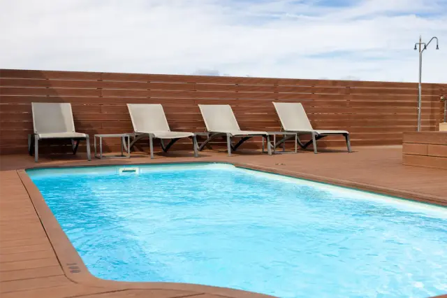 Piscina rectangular con agua azul clara rodeada de una terraza de madera.