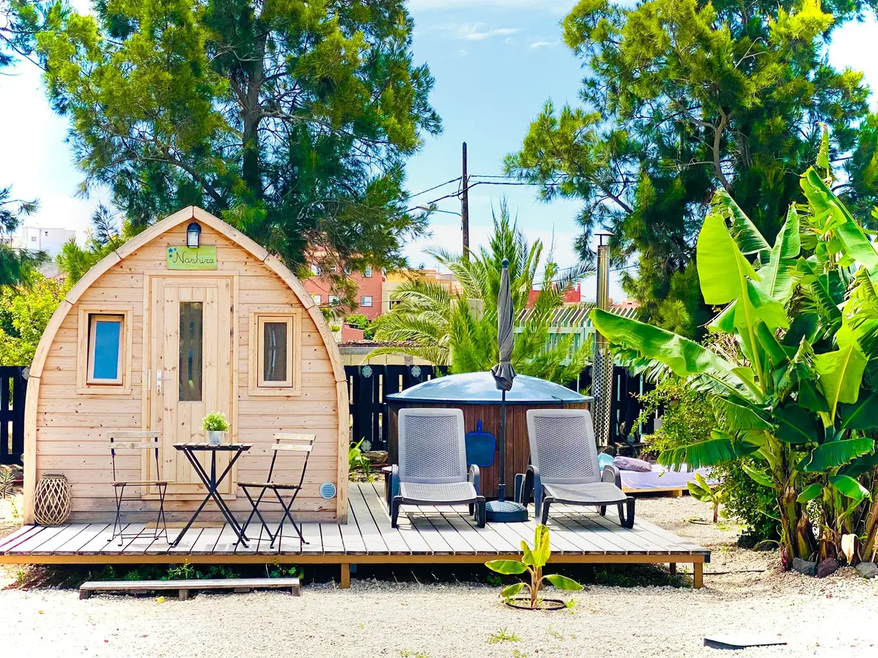 Vista exterior de una cabaña de madera con forma de barril en un entorno natural, con terraza de madera que incluye