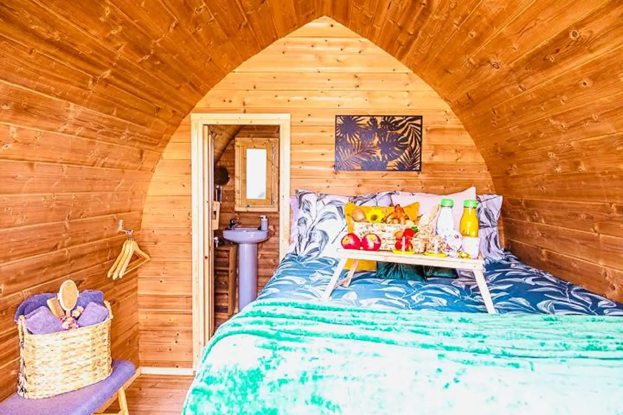 Interior de una habitación abovedada de madera con una cama grande cubierta por una colcha verde y azul, bandeja