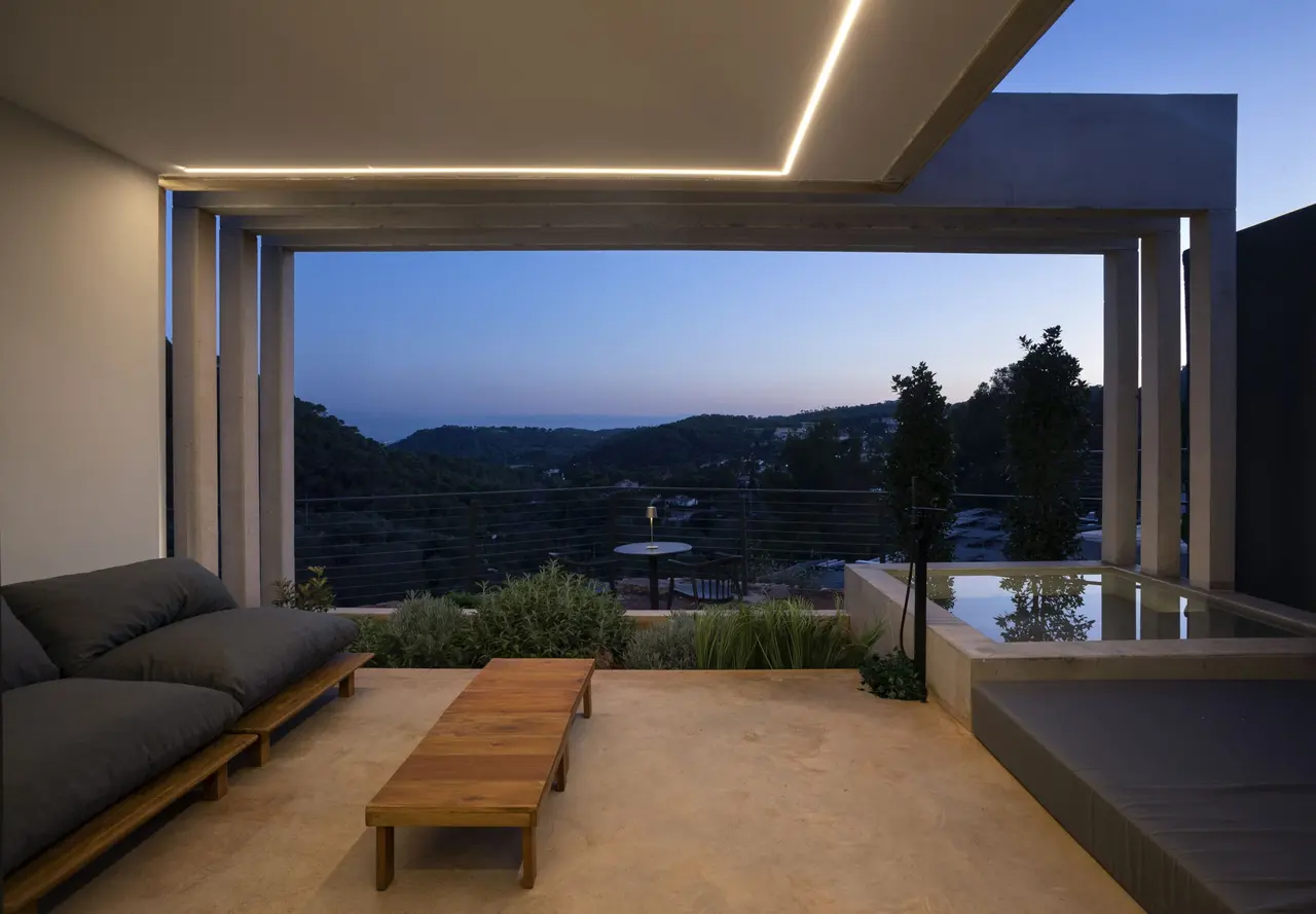 Vista de una piscina privada rectangular en una terraza moderna al atardecer, con sofás y mesas de madera en primer