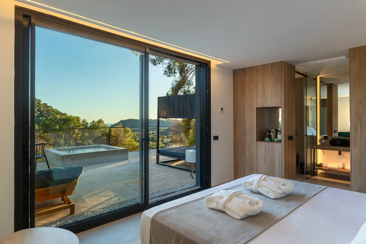 Vista desde el interior de la villa hacia la terraza con piscina privada climatizada rectangular, rodeada de paisaje
