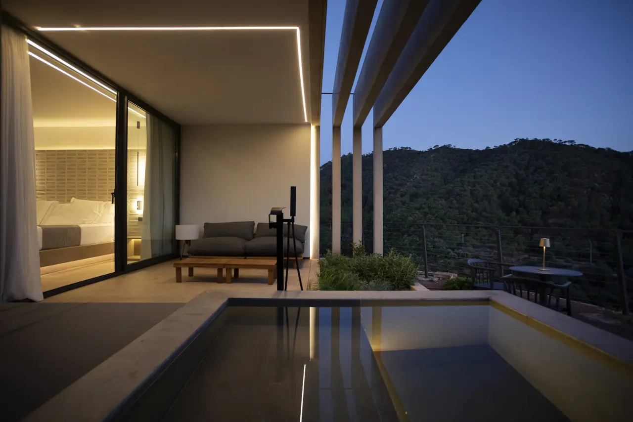 Piscina privada rectangular en terraza exterior de villa al atardecer, con sofá, mesa y vistas a montañas boscosas.